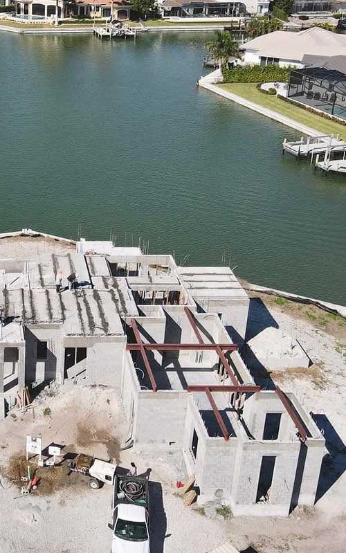 A concrete building under construction near a waterfront, with steel beams exposed and construction materials on site.